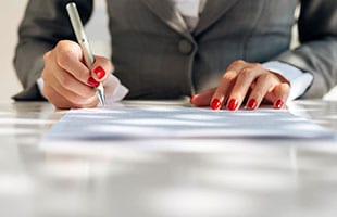 A person writing on paper with red nails.