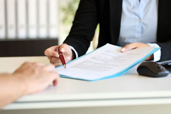 A person holding a pen and paper in front of another person.